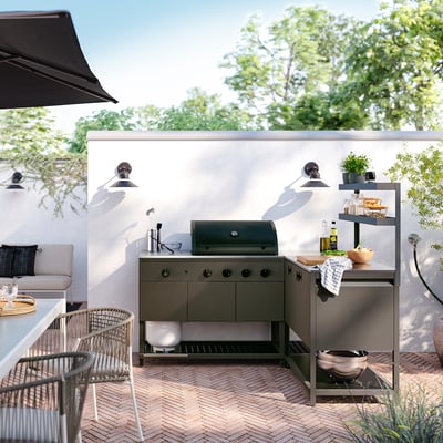 Liten, grön BÅTSKÄR utekök med hyllor och gasolgrill. Perfekt för matlagning och förvaring i ett snyggt, organiserat utomhusutrymme.