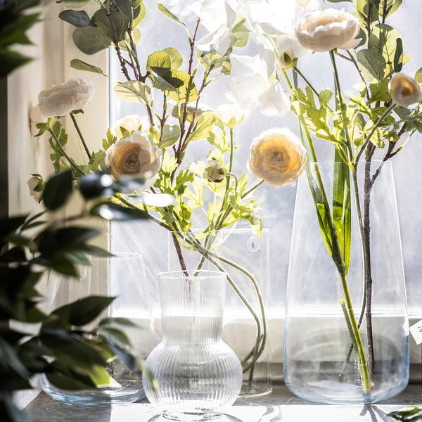 Tre glasvaser med vita blommor på en solbelyst fönsterbräda.