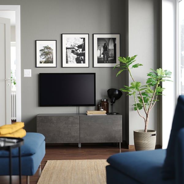 Modernt vardagsrum med grå BESTÅ tv-bänk, svart plattskärms-tv, blå stolar och tre inramade foton ovanför.