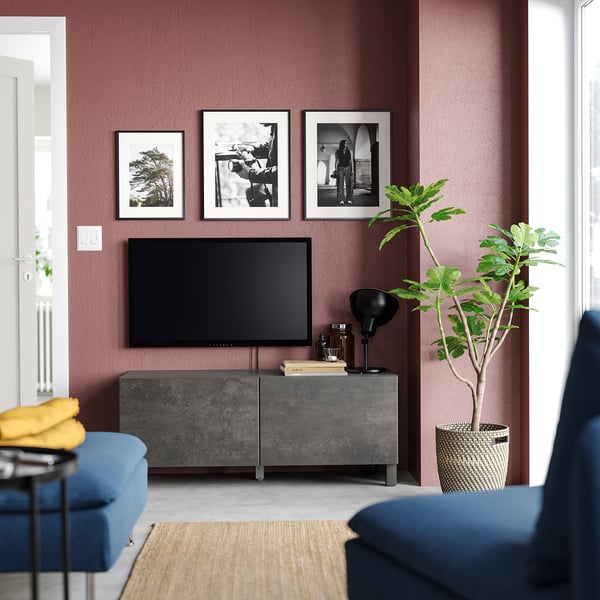 Modernt vardagsrum med bruna väggar, blå möbler, grått tv-ställ, plattskärms-tv, svart lampa, gul filt och stor växt.