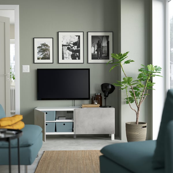 Modernt vardagsrum BESTÅ tv-bänk med justerbara hyllor, dolda kablar och mjukstängande dörrar. Den är monterad nära en grön vägg med inramade foton.