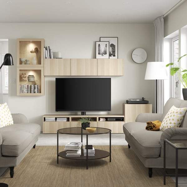 Modernt vardagsrum med trä och grå inredning, tv, grå soffor, svart soffbord, lampa, stort fönster, klocka och konst.