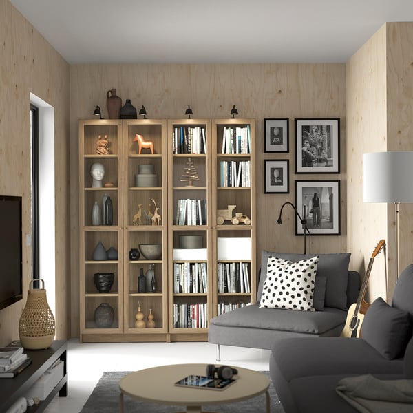 Modernt vardagsrum med bokhyllor från BILLY, grå soffa, runt bord och vägglampor. Svartvita foton på väggen.