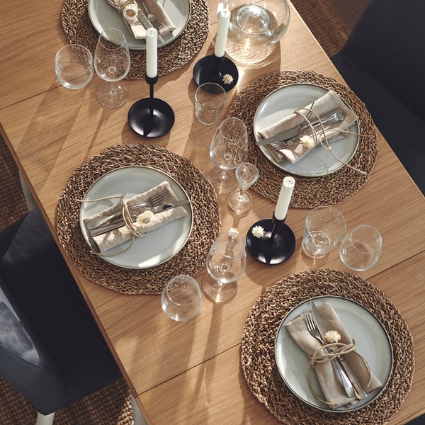 DANDERYD bordsset för fyra personer med gröna tallrikar, rottingmattor, silverbestick, glas, ljus och servetter. Rustik design.