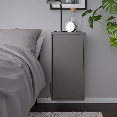 Modernt grått vägghängt skåp, en del av en ikea EKET serie, med en klocka och en lampa, monterade bredvid en säng.