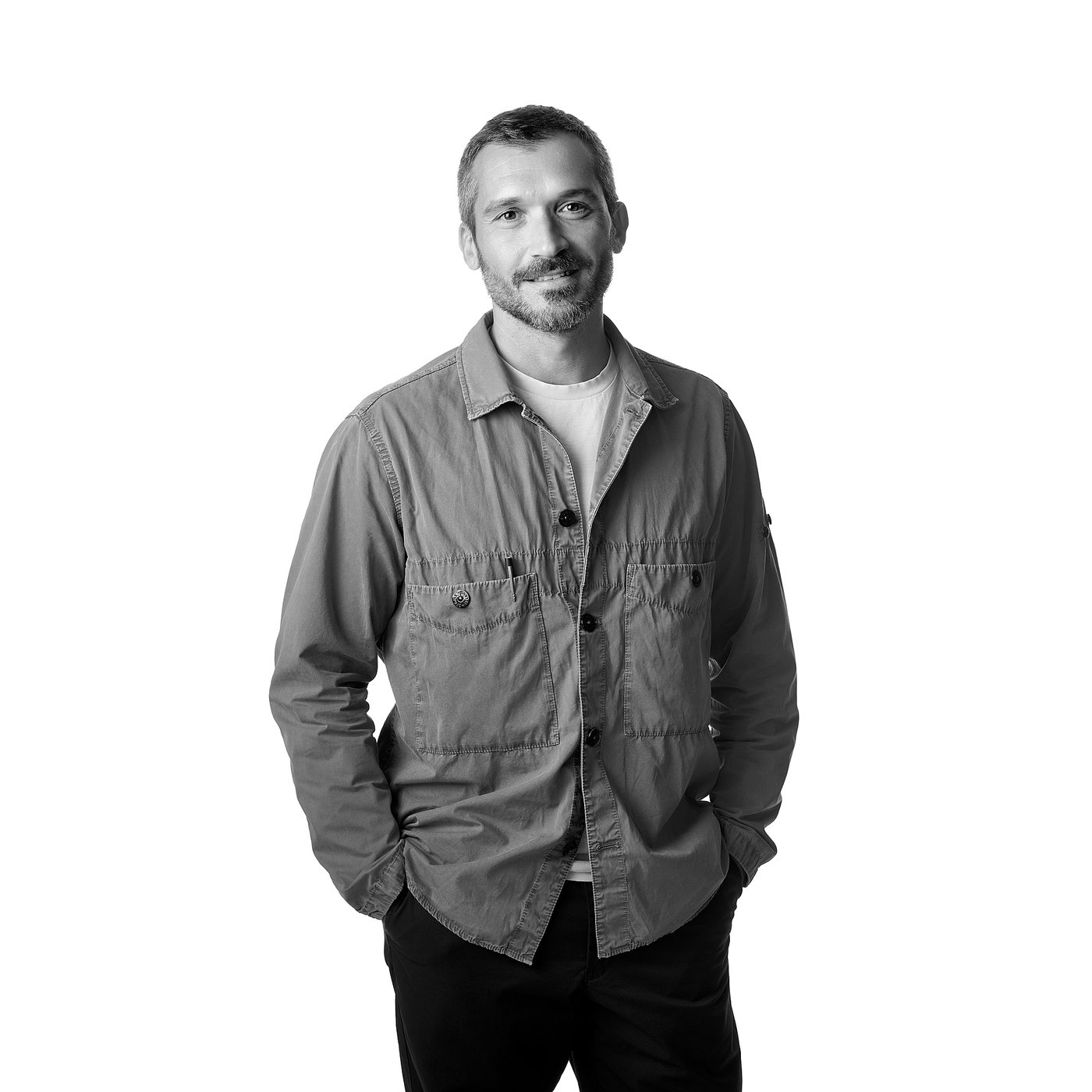 Svartvitt porträtt av Gio Tirotto med händerna i fickorna, klädd i en långärmad skjorta och mörka byxor.