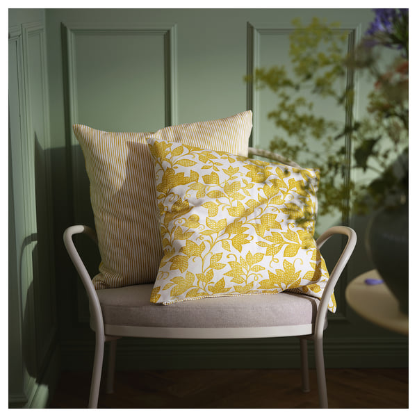 Två klargula och vita kuddar på en vit stol, en med blommönster, den andra randig.
