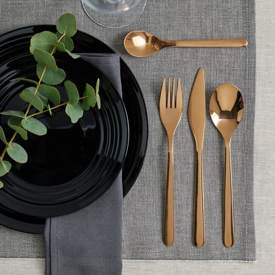 Elegant FÖRNUFT bestickset: svarta handtag, glänsande guld, rostfritt stål, enkel design. Välplacerad på grå duk, bredvid svart tallrik och ilägg.