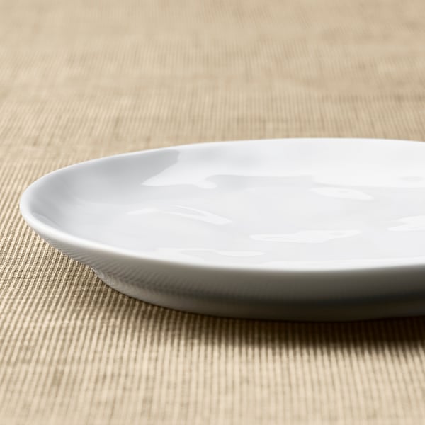 Vit porslinstallrik med en texturerad, blank yta vilar på ett lätt träbord. Lyfter fram dess handgjorda känsla och hållbarhet.