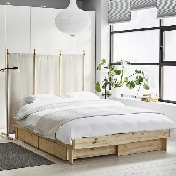 Modernt sovrum med GLAMBERGET träsäng, vita sängkläder, hängande lampa och fönsterväxt.