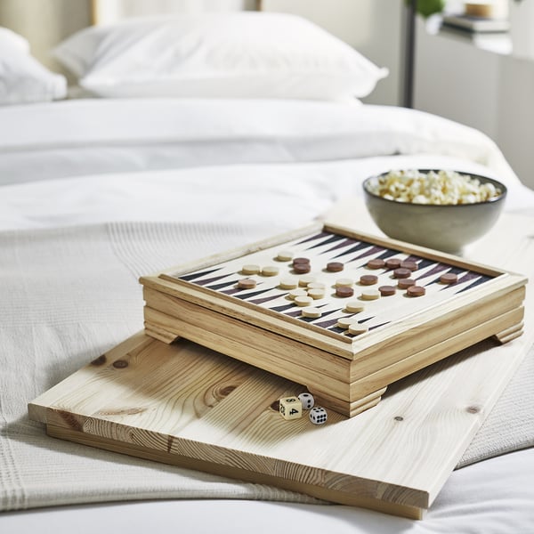 På en säng ligger ett brädspel i trä och popcorn.
