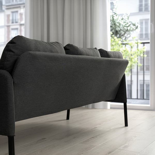 Modernt minimalistiskt vardagsrum med kol GLOSTAD soffa, eleganta svarta ben, plyschkuddar, placerad nära stort fönster, litet mot väggen.