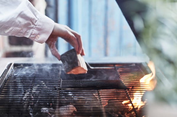Handgrillar mat på modern silvergrill. Lågor synliga under metallgaller.