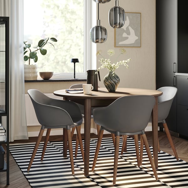 Modern matplats med runt bord, grå stolar, randig matta och vita blommor; ljust, naturligt ljus.