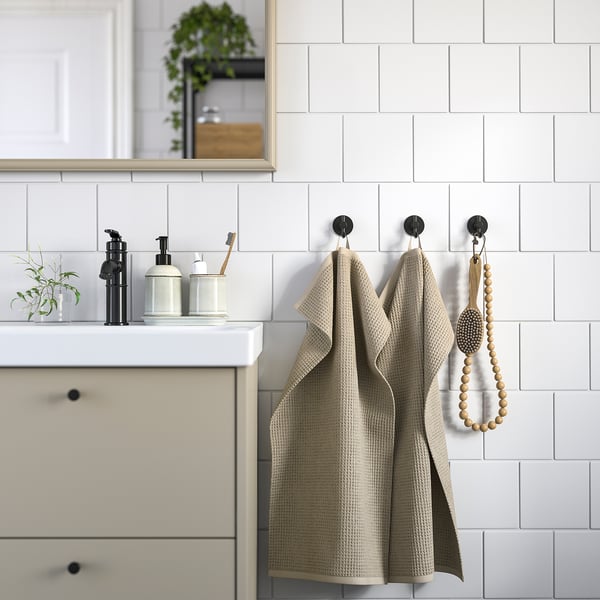 Modernt badrum med beige handdukar, vit handfat, svarta dispenser och växt.