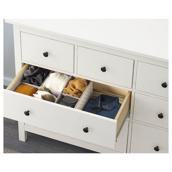 Vit byrå med svarta knoppar, som visar organiserade kläder i tre lådor. Ingår i ikeas HEMNES serie sovrumsmöbler.