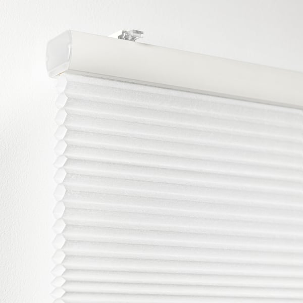 Vit cellulär persienn installerad mot en vit vägg, delvis nedrullad för ljuskontroll, med en synlig draglinaslits och fästen.