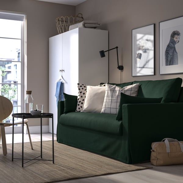Modernt vardagsrum med grön HYLTARP soffa, stor konst, elegant bord, mysig matta och vit förvaringsmöbel.