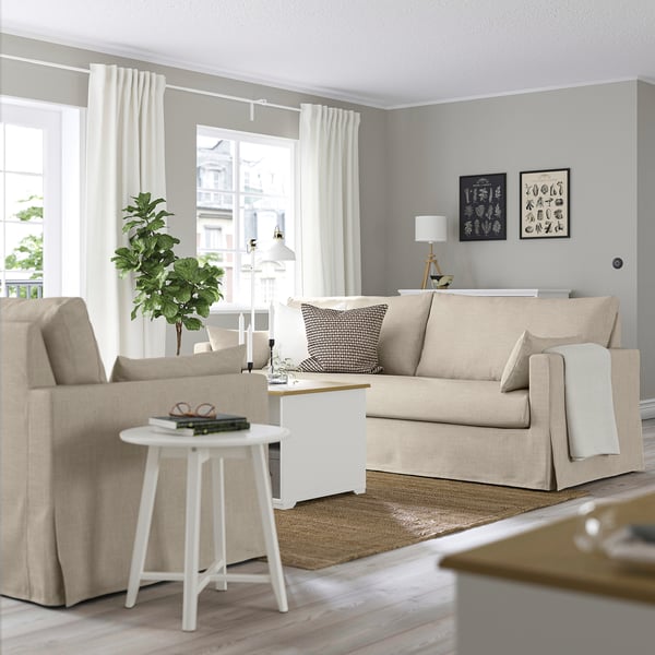 Modernt vardagsrum med HYLTARP beige soffa, fotoramar, vit matta, sidobord och lampa.