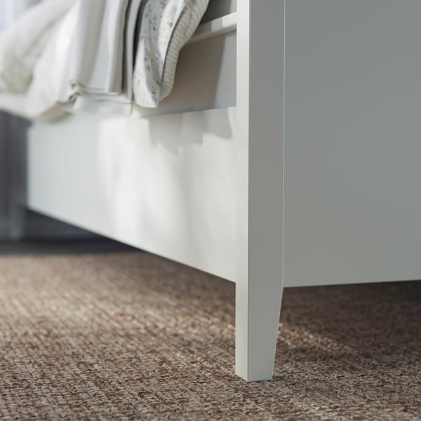 Närbild på IDANÄS vita sängstomme med hantverksmässiga ben och öppen låda.