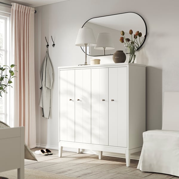 Modern entré med vitt IDANÄS-skåp, spegel, lampor, blommor, klädkrokar och ljusrosa gardiner.
