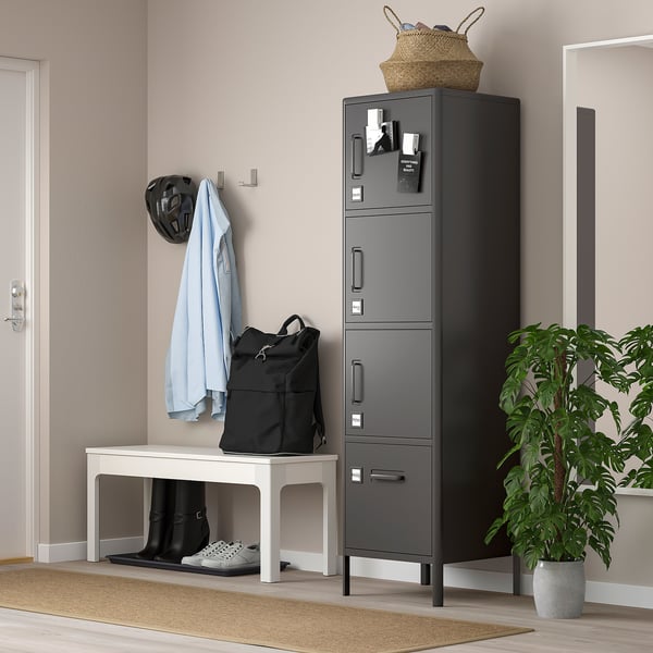 Ett IDÅSEN-skåp i grått, tillverkat av stål, med flera fack. Den står högt med en elegant design bredvid en vit bänk och en krukväxt.