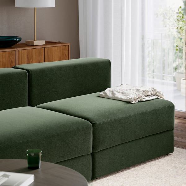 Grön JÄTTEBO modulsoffa med förvaring; beige filt på ottoman; Träskåp och lampa i närheten.