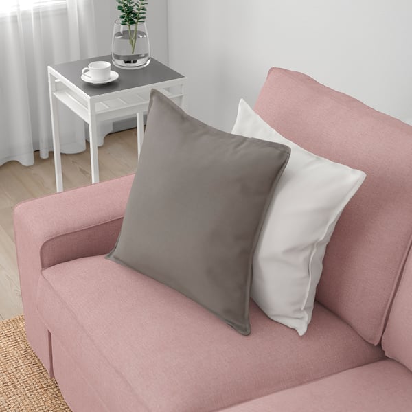 En rosa soffa med grå och vita kuddar som visar upp sina rymliga och bekväma sittplatser, perfekt för avkoppling.