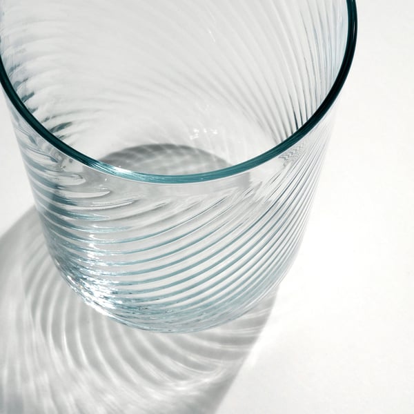 Närbild av ett elegant, klart glas med en slät exteriör och texturerad interiör, som kastar intrikata skuggor och framhäver dess delikata kvalitet.
