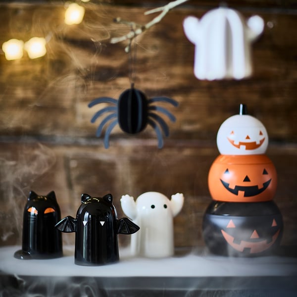 Halloweendekorationer: staplade pumpaburkar, svarta och orange, med fladdermus-, katt- och spökfigurer; burkar mindre än figurer.