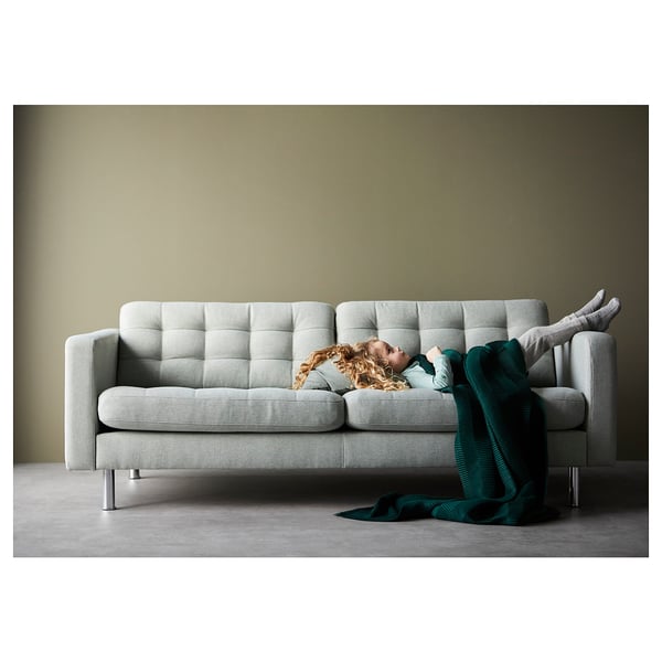 Person som sover på ljusgrå vadderad soffa med grön filt, benen upp, modern design, mysigt vardagsrum.