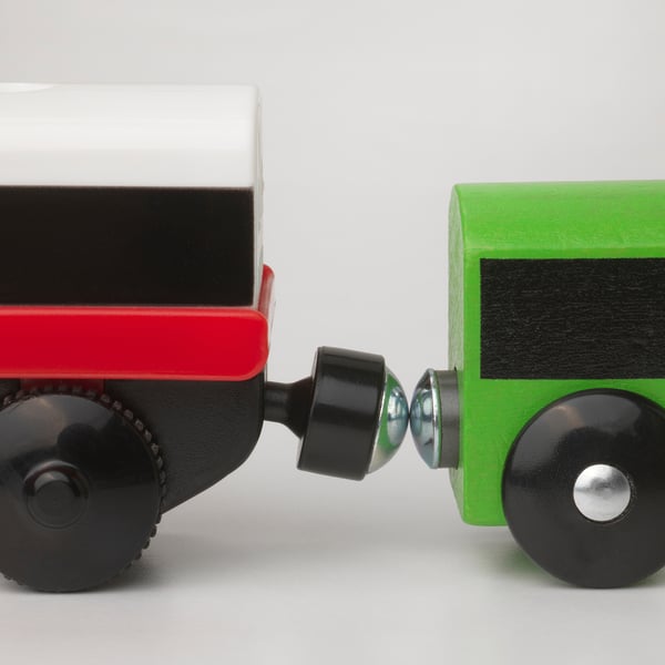 Childs tågmotor i trä, röd och grön, ansluten med en svart koppling, på vit yta.