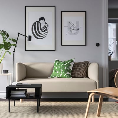 Modernt vardagsrum med beige soffa, gröna kuddar, abstrakt konst, växt, böcker, stol.