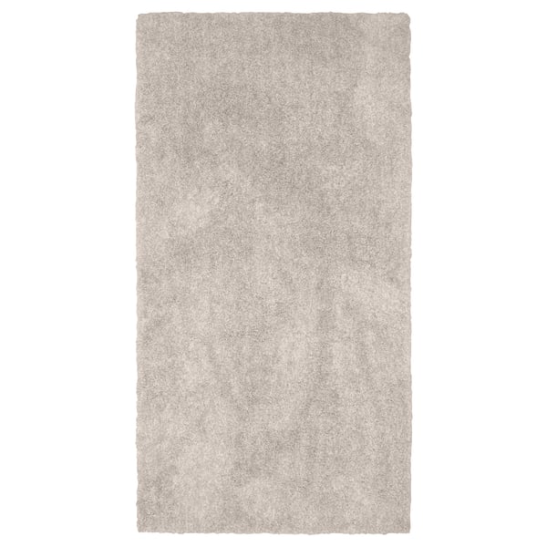 En rektangulär, beige matta LINDKNUD. Den är tillverkad av återvunnen polyester och har en mjuk, plyschyta som är idealisk för sovrum.