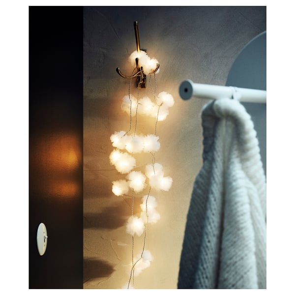 Dekorativa vita LED-lampor hänger från en guldkrok nära en handduk på en vit stång och skapar en mysig atmosfär.