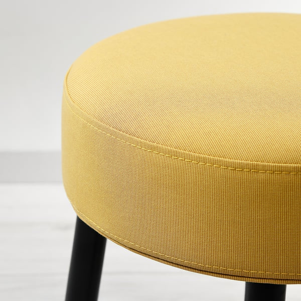 Närbild av en modern, rund, gul stoppad pall med eleganta svarta ben, som visar upp sitt kvalitetstyg och sin rena design.