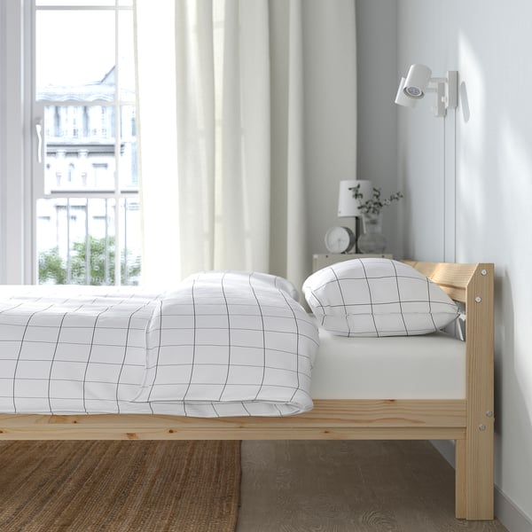 Sängram i trä med vitt galler sängkläder nära ett fönster, upphöjda för förvaring.