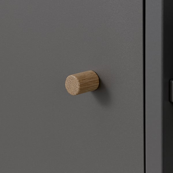 Ett elegant, modernt möbelhandtag i cylindriskt trä. Mot en slät, grå yta framhävs dess naturliga, strukturerade utseende.
