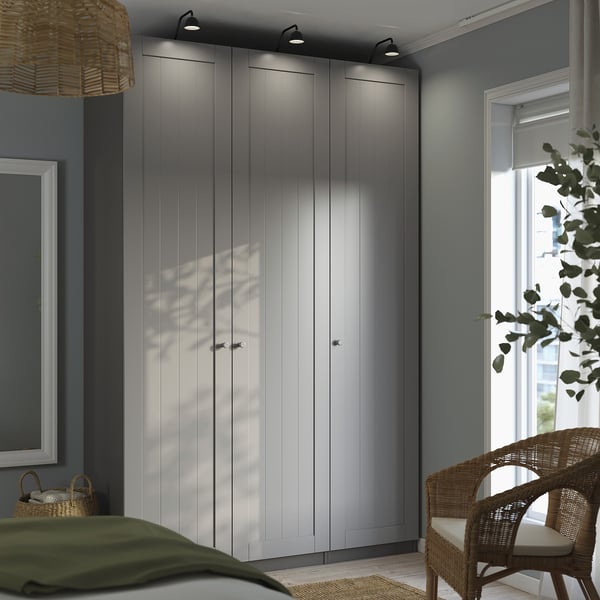 Modern sovrum hög grå PAX garderob med elegant design, matchande korgstol och grön filt på sängen.