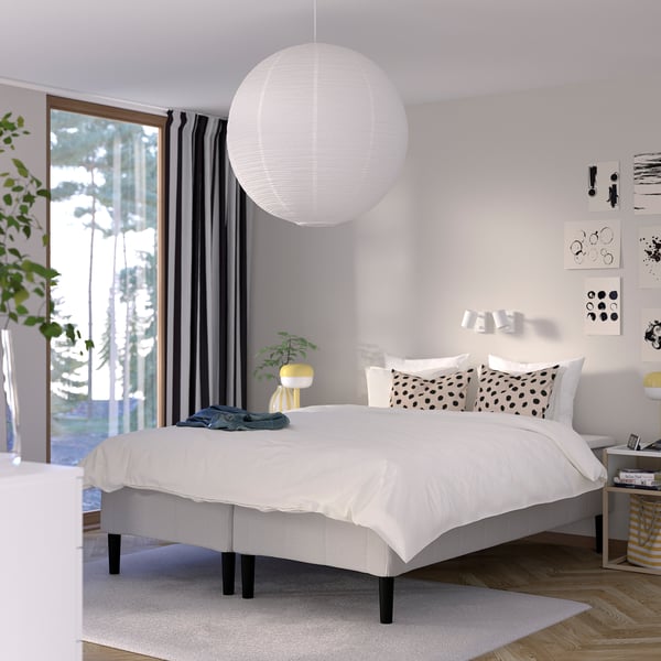 Modernt minimalistiskt sovrum med vit säng RÅHOLMAR , stort runt ljus, svarta gardiner, prickiga kuddar, nattduksbord, väggkonst och växter.