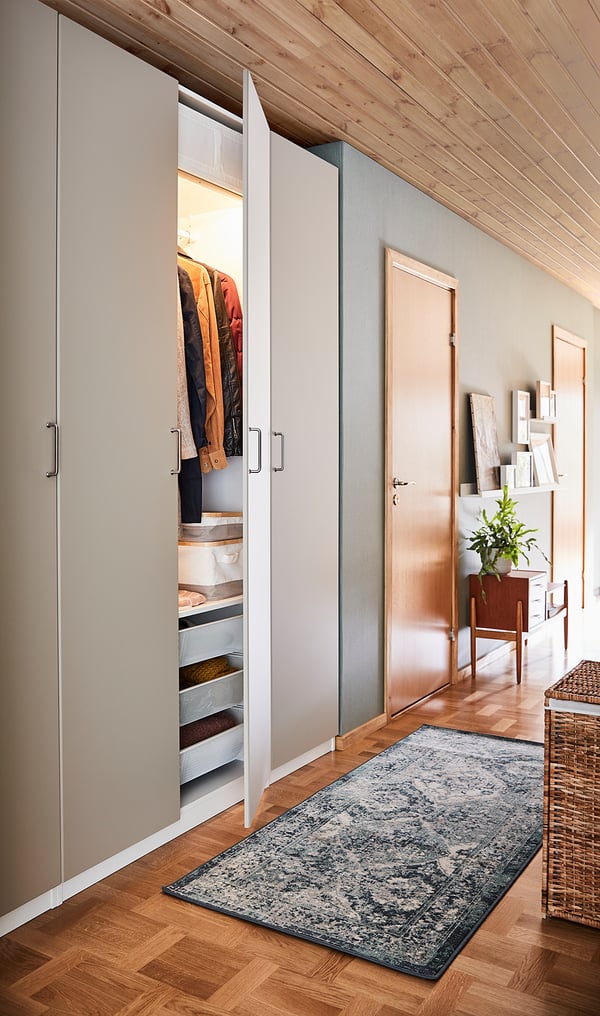 Modern garderob med REINSVOLL gråbeige dörr, minimalistisk design, öppna avslöjande kläder, set på trägolv, blå matta.