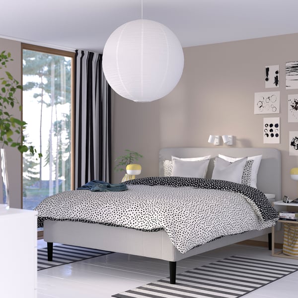 Minimalistiskt sovrum med sängen RISHÖJDEN , svartvit inredning, mjuk matta, stort fönster, växt.