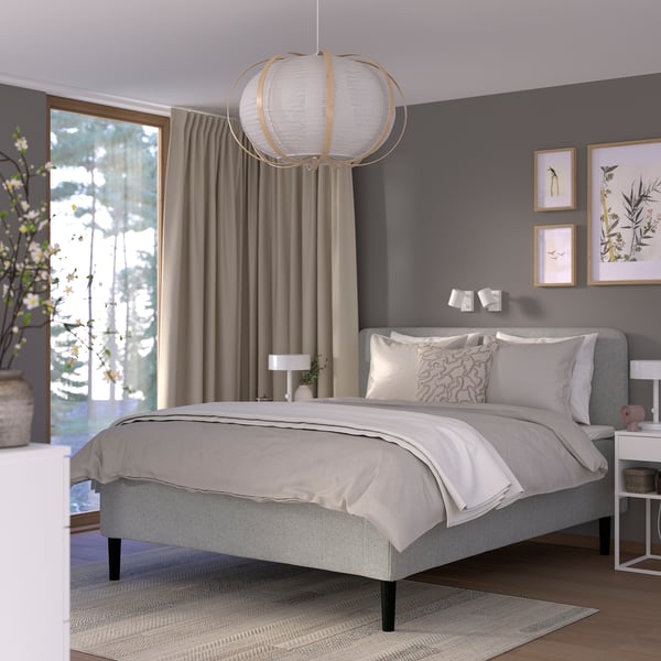 Modernt minimalistiskt sovrum RISHÖJDEN grå säng, hängd lampa, inramad konst och växt. Mjuka gardiner och trägolv förstärker den mysiga men ändå eleganta atmosfären.
