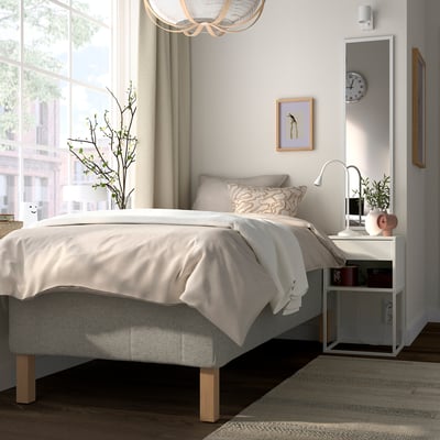 Modernt sovrum: låg grå säng med vita sängkläder, nattduksbord i trä, guldaccenter, stort fönster, beige gardiner, väggklocka och minimalistisk inredning.