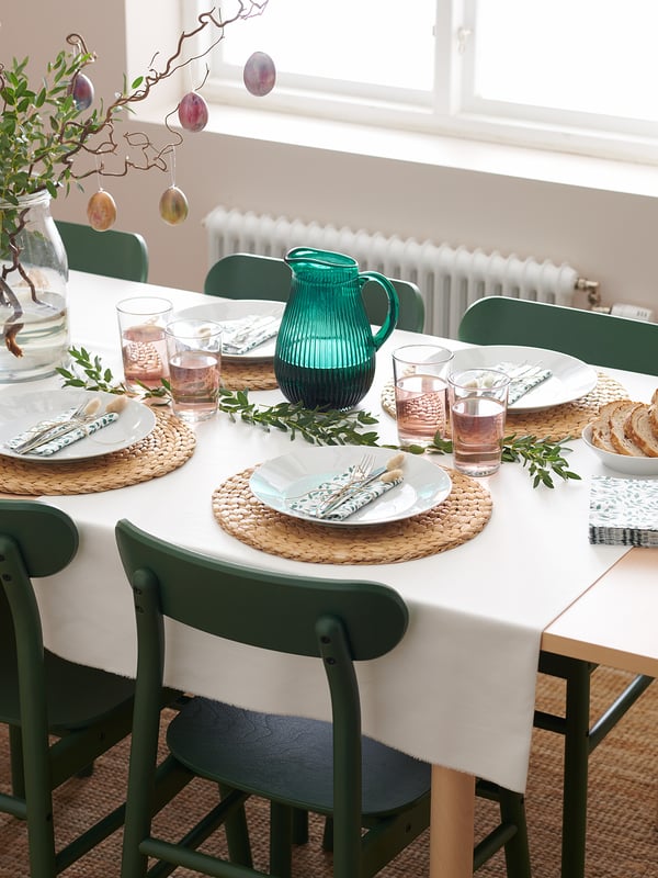 Matbordsset med vita tallrikar, gröna stolar, glaskanna, servetter och bestick. Enkla och eleganta dukningar.
