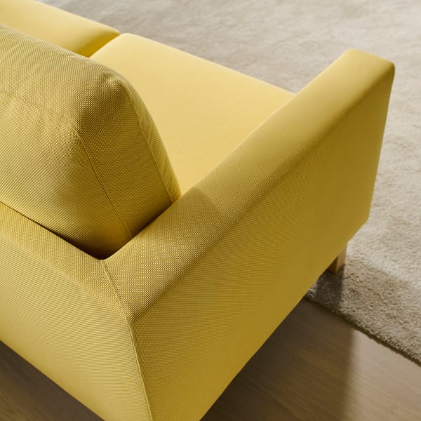 Gul soffa på nära håll, med mjuka kuddar och en stadig design på trägolvet.
