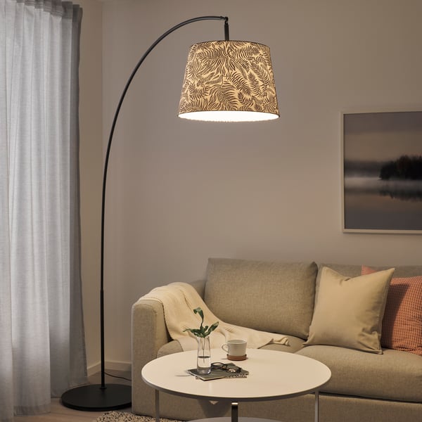 Svart SKAFTET golvlampa med zebramönstrad skärm hänger över beige soffa och vitt bord. Mjuk, varm belysning lyser upp det mysiga vardagsrumshörnet.