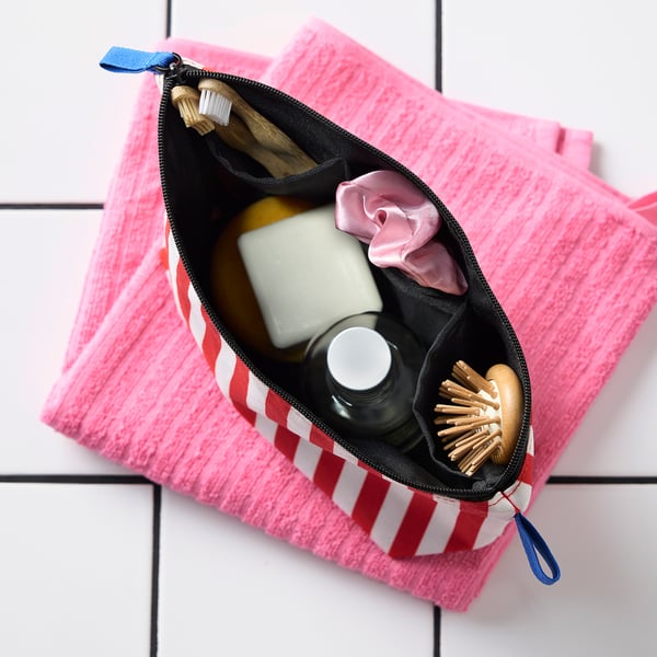 Röd/vitrandig necessär med blå dragkedja på rosa handduk.