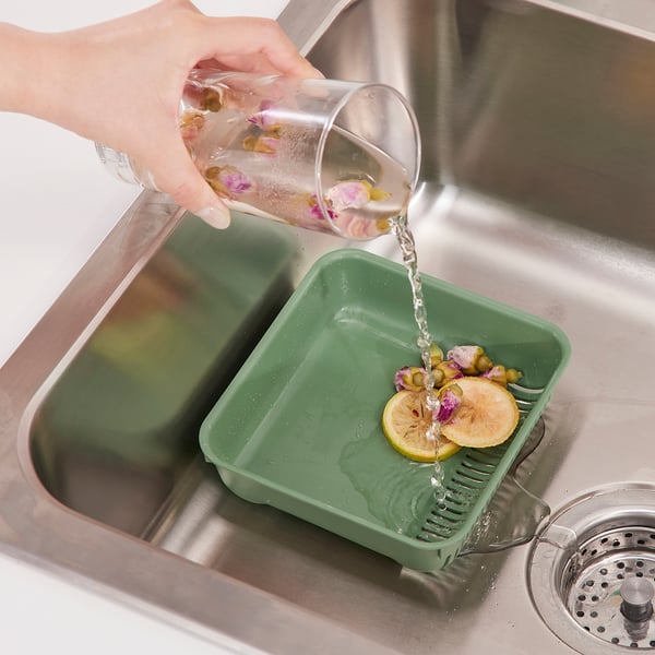 Häller för hand vatten från burken i den gröna diskbänken med citronskivor och blommor, vilket visar hur du samlar in matavfall.