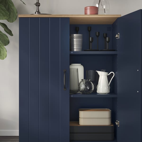 Marinblått skåp med ekskiva som visar vaser, ljusstakar och askar. Topppanel fäst på väggen.